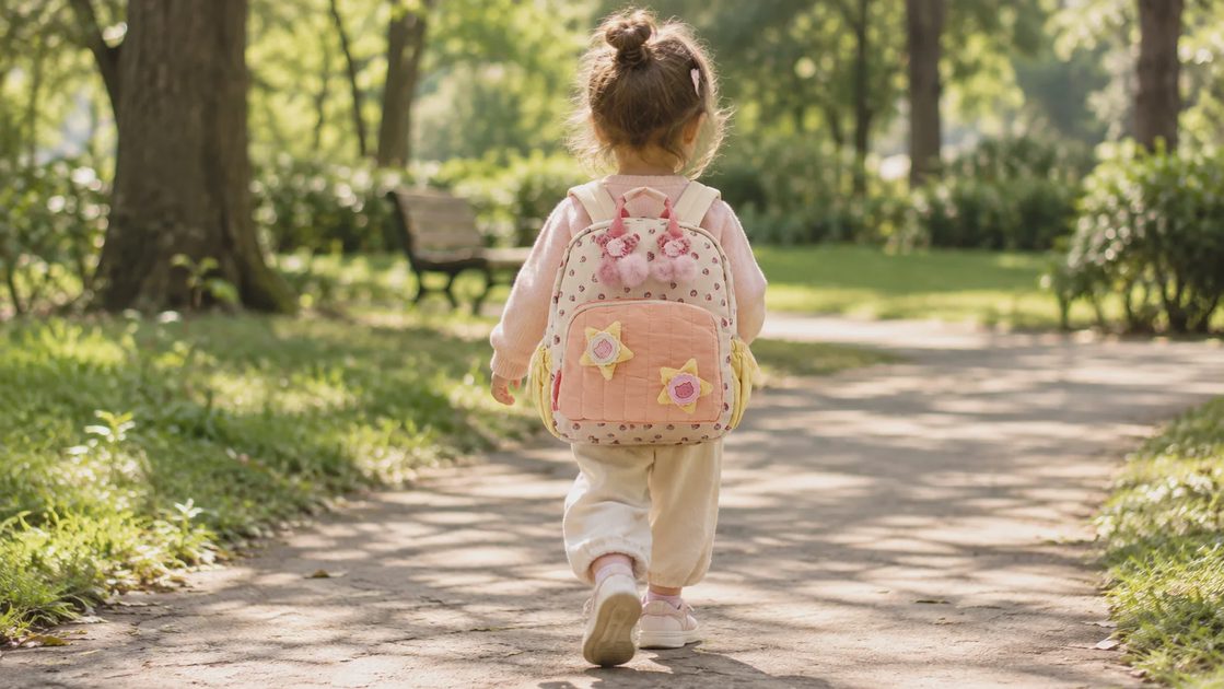 Toddler walking along a park path wearing a strawberry print backpack, seen from behind